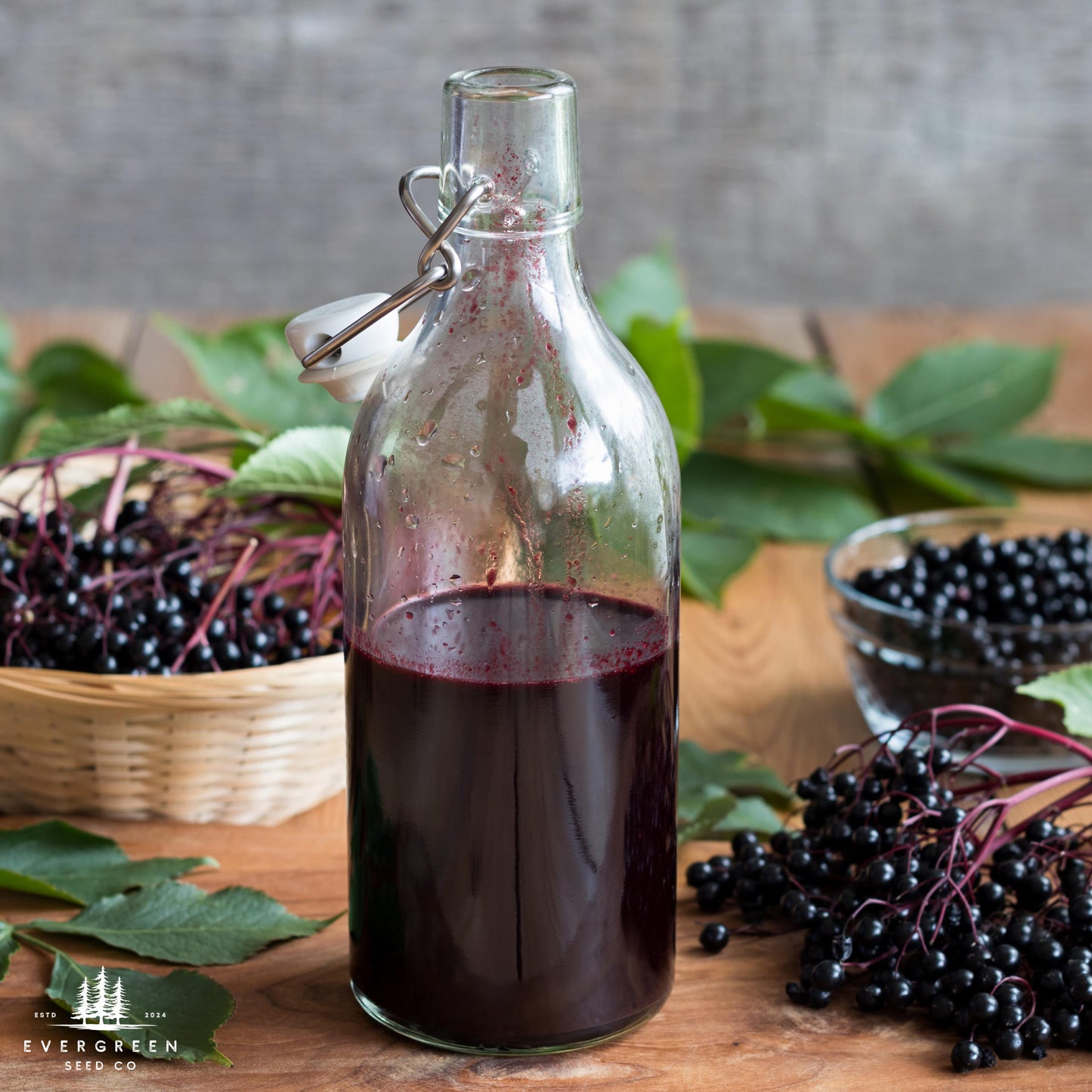 Bottle of dark liquid elderberry syrup with elderberries and leaves on a wooden surface.