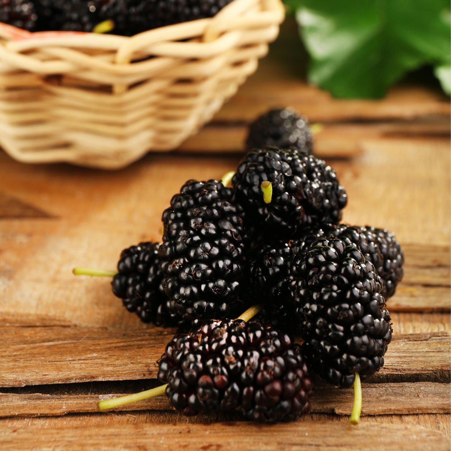 Cluster of mulberries on a wooden surface with a basket in the background.